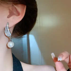 Close-up of elegant wing-shaped earrings with sparkling diamonds and a pearl drop
