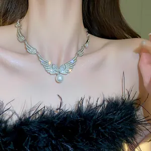 Close-up detail of a rhinestone winged pearl necklace worn by a model with black feathers