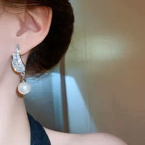Close-up view of a model wearing elegant silver wing earrings with white pearl drops.