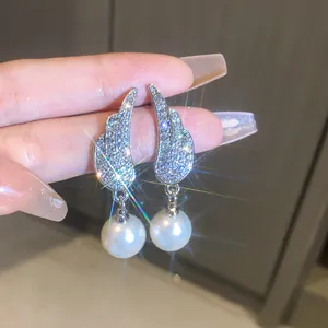 Close-up of elegant silver wing earrings with sparkling rhinestones and white pearl drops