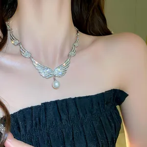 Detail view of a French style necklace with rhinestone angel wings and a pearl pendant.