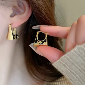 Detailed view of vintage gold hoop earrings with black floral enamel inlay worn on ear