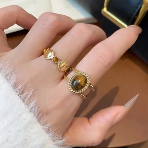 Primer plano de anillos chapados en oro de 18k con piedra ojo de tigre en la mano
