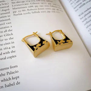 Vintage gold-tone hoop earrings with black enamel floral design on aesthetic book page