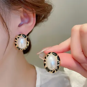 Close-up of vintage oval earrings with white pearl center and black enamel border detail.