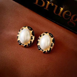 Detailed shot of vintage-style oval earrings with white pearl and black enamel accents