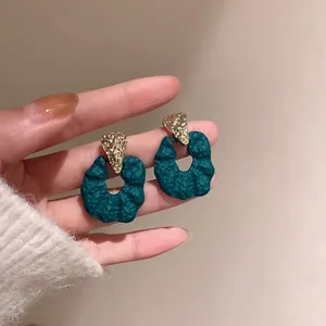 Close-up of irregular geometric textured earrings in gold and dark green