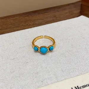 Primer plano de un anillo abierto bañado en oro de 18k con tres piedras turquesas