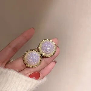 Close-up of round iridescent stud earrings with gold-tone textured border details