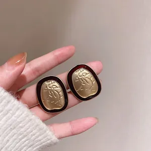 Close-up of irregular geometric stud earrings with matte gold and dark red enamel detail