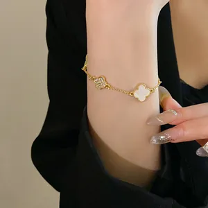 Close-up detail of a gold clover bracelet with rhinestone and white inlay