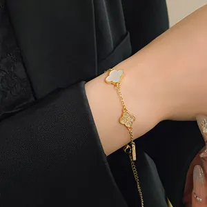 Detailed close-up view of a gold chain bracelet featuring rhinestone and white clover charms.