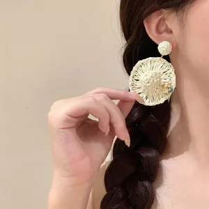 Macro detail of hand-woven straw sun hat earrings with flower decoration on model