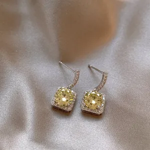 Close-up of elegant square zircon drop earrings on soft champagne satin fabric