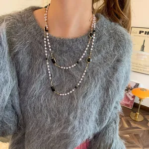 Vintage double-layered long pearl necklace with black stones worn on a grey fuzzy sweater