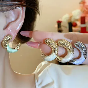 Close-up of elegant C-shaped hoop earrings with gold texture and pastel enamel finish.