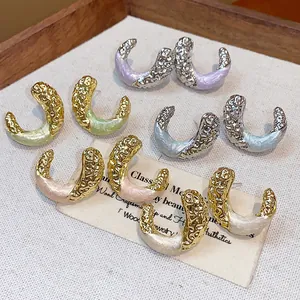 Detailed view of wrinkled C-shaped earrings with drip oil finish in a wooden tray.