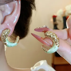 Macro detail of C-shaped wrinkled gold earrings with light green enamel drip finish