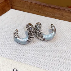 Detailed macro view of textured metallic silver and light blue drip oil C-shaped stud earrings