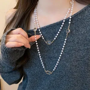 Elegant long layered pearl necklace with clear crystals worn over a grey knit sweater.