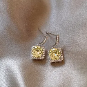 Detailed macro shot of square halo drop earrings with yellow zircon on satin silk background