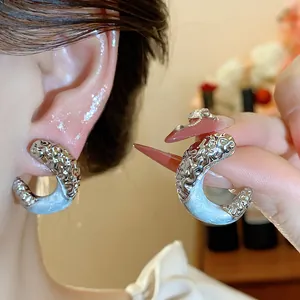 Close-up of silver C-shaped earrings with wrinkled texture and light blue enamel detail.