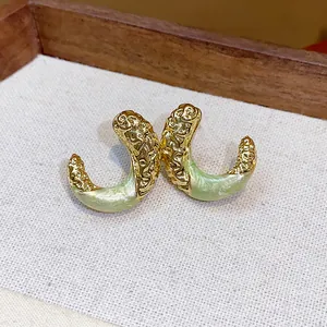 Close-up view of elegant gold wrinkled C-shape earrings with light green enamel drip finish