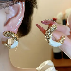 Detail view of stylish C-shaped earrings featuring gold wrinkled texture and white enamel