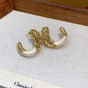 Close-up detail of stylish gold-toned wrinkled C-shape stud earrings with cream enamel