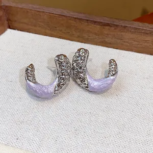 Close-up of wrinkled C-shaped earrings with lavender enamel and silver metallic finish