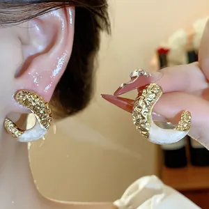 Detailed view of gold pleated C-shaped earrings with pearlescent white enamel finish.