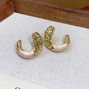 Detailed macro view of gold-tone wrinkled C-shaped stud earrings with pink enamel detail