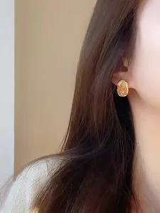 Close-up view of elegant gold geometric stud earrings with crystal texture on a model