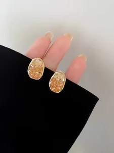 Detailed macro view of elegant gold geometric stud earrings with amber crystal inlay