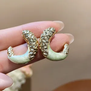 Close-up of elegant C-shaped stud earrings with gold crinkled texture and pale green enamel