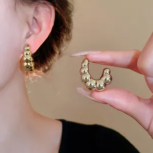 Detalle de pendientes de aro de metal dorado retorcidos en forma de C en una modelo