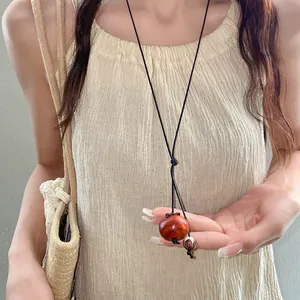 Dettaglio di una collana con ciondolo in legno a forma di caco su cordino