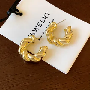 Primer plano de pendientes de tuerca de metal dorado retorcido en forma de C en tarjeta