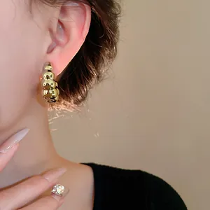 Primer plano detallado de pendientes de metal dorado en forma de C torcida en la oreja de mujer