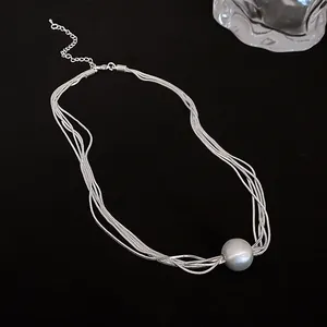 Close-up of a minimalist silver multi-layered necklace with a large round metal ball pendant