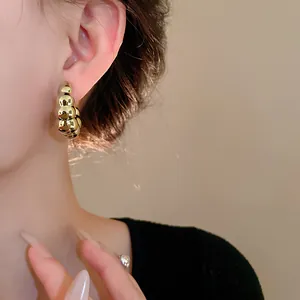 Primer plano de un elegante pendiente de aro de metal dorado retorcido en forma de C.