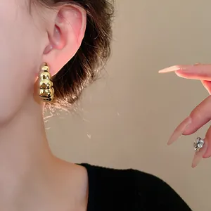 Vista detallada de un pendiente de metal dorado retorcido en forma de C en la oreja.