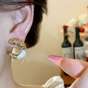 Close-up of golden wrinkled C-shaped earrings with white enamel detail on ear