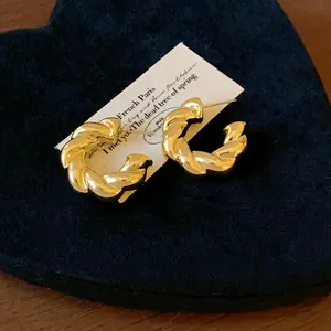 Detalle de pendientes dorados retorcidos en forma de C en tarjeta de regalo