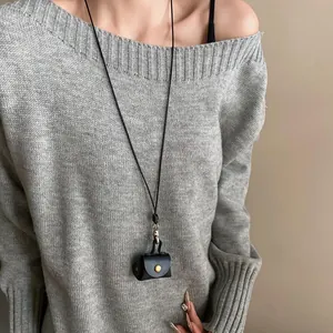 Close-up detail of a minimalist black leather mini earphone pouch necklace worn on a grey sweater