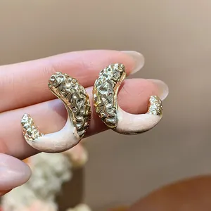 Macro view of wrinkled texture C-shaped earrings with soft pink enamel finish.