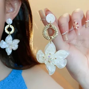 Detailed macro view of elegant white resin flower earrings with textured gold hoops.
