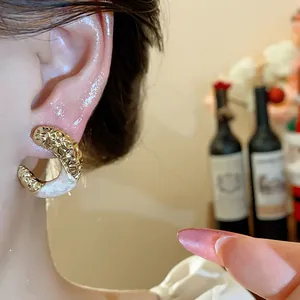 Detail of textured C-shaped gold stud earring with pearlescent enamel drip oil