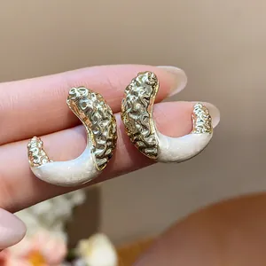 Detail shot of elegant gold crinkled C-shaped stud earrings with white pearl enamel finish