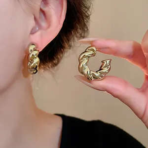 Primer plano de elegantes pendientes de aro metálicos retorcidos en C dorados en oreja